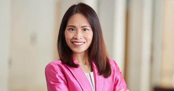 Christie K. Chung smiles at the camera. She is wearing a bright pink blazer over a light top, standing with her arms crossed in a softly lit indoor space.