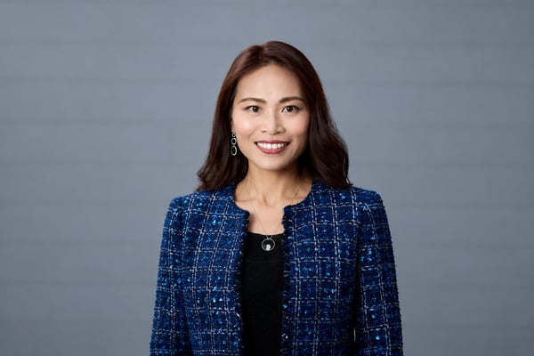 Professional headshot of Dr. Christie Chung smiling and facing the camera, wearing a blue patterned jacket and black top against a neutral gray background.