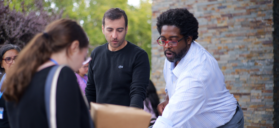 A Writing Studio staff member engages with participants at an outdoor event, speaking with attendees and handing out materials, with others gathered nearby.