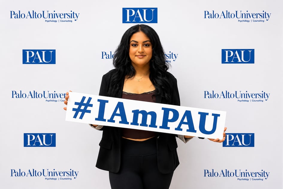 Shirin Aghakhani poses in front of a Palo Alto University backdrop holding an "#IAmPAU" sign.